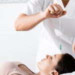 hypnotist standing near woman and holding green stone above her face