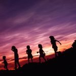 silhouettes of children camping down a hill at sunset